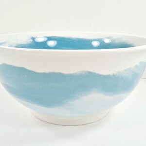 May include: White ceramic bowl with a wide, rounded shape. The bowl features a watercolour-style design with a band of light blue around the middle, transitioning to white at the top and bottom. The interior is also light blue.