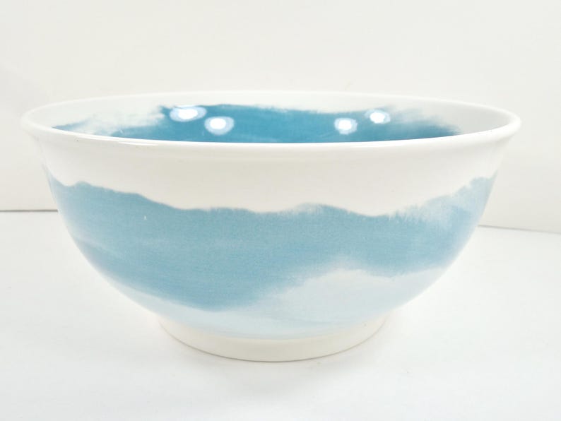 May include: White ceramic bowl with a wide, rounded shape. The bowl features a watercolour-style design with a band of light blue around the middle, transitioning to white at the top and bottom. The interior is also light blue.