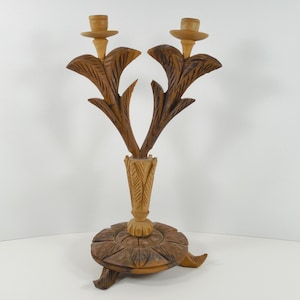 May include: A wooden candle holder with two candle cups, carved in the shape of stylized palm leaves. The base is also carved with a floral design.