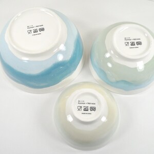 May include: Three ceramic bowls in different sizes, featuring white interiors and painted exteriors in blue and green hues. The bowls have a glossy finish and are set on a white surface. Measurements are in cm.