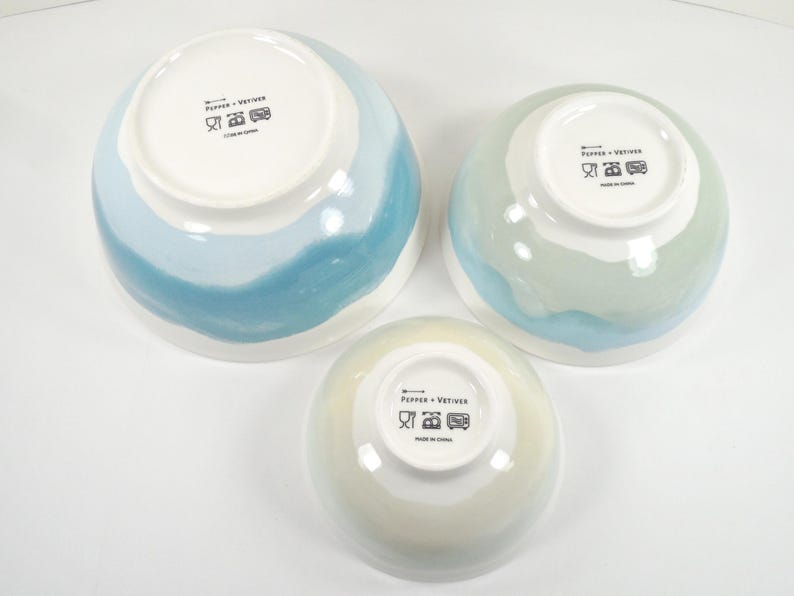 May include: Three ceramic bowls in different sizes, featuring white interiors and painted exteriors in blue and green hues. The bowls have a glossy finish and are set on a white surface. Measurements are in cm.