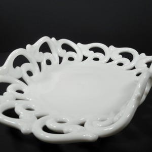 May include: A white porcelain bowl with a decorative, openwork design. The bowl is oval shaped and has a scalloped edge.