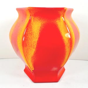 May include: A vibrant, hexagonal-based vase with a glossy finish. The vase features a striking color scheme of red and yellow, with the yellow streaks creating a flame-like pattern. The vase has a wide opening and a rounded body.