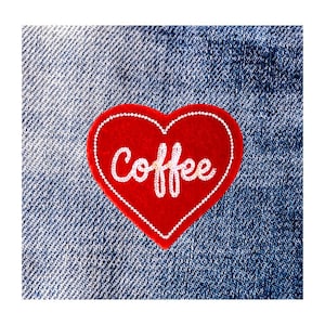 May include: A red heart-shaped patch with the word "Coffee" embroidered in white cursive. The patch has a white stitched border and is set against a blue denim background.