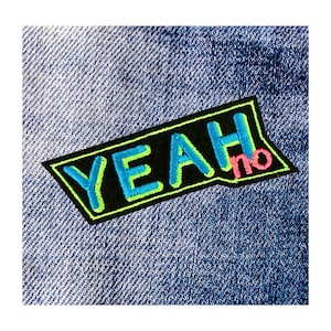 May include: A rectangular patch with the word "YEAH" in blue, outlined in neon green, and the word "no" in pink. The patch is on a black background with a neon green border, set against a blue denim fabric.