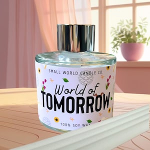 May include: A clear glass candle jar with a silver lid, labelled "World of Tomorrow" with floral and leaf accents. The label also reads "Small World Candle Co." and "100% Soy Wax." A white diffuser stick is in the foreground.