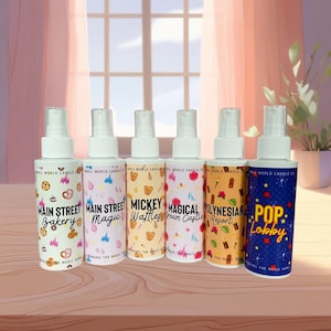 May include: Six white spray bottles with colourful labels. The labels feature text like "Main Street Bakery," "Mickey Waffles," and "Pop Lobby." The bottles are arranged in a row against a soft, blurred background.