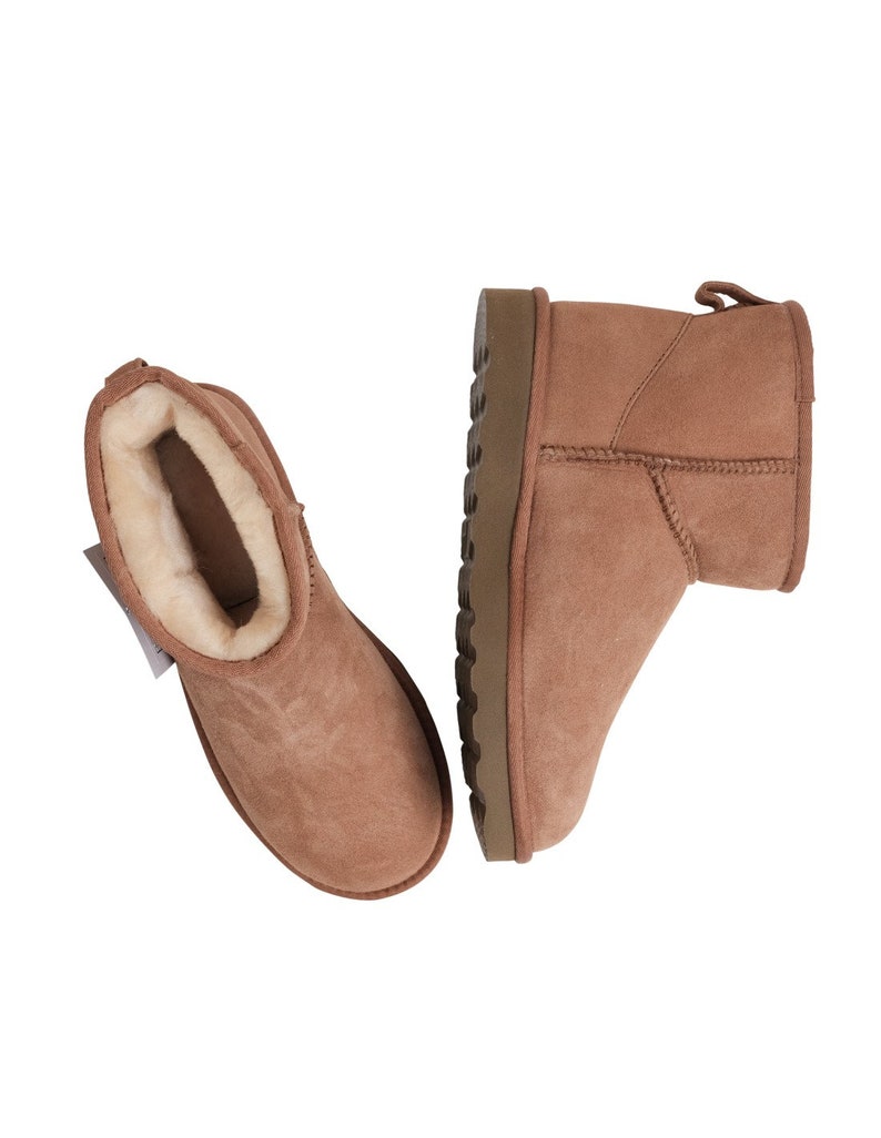 May include: A pair of brown suede ankle boots with a sheepskin lining. The boots have a brown rubber outsole.