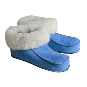 May include: A pair of blue suede slippers with a thick, fluffy white sheepskin collar. The slippers have a rounded toe and are designed for indoor wear. The soft, plush material provides warmth and comfort.