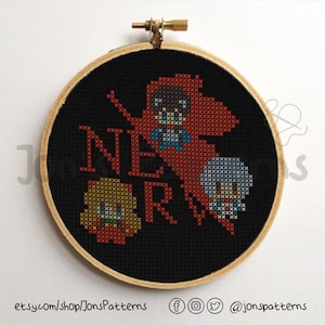 May include: A black embroidery hoop with a cross-stitch design featuring the characters from the anime series Neon Genesis Evangelion. The characters are depicted in pixelated form and the text "NERV" is stitched in red and white.