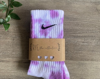 May include: Purple and white tie-dye socks with a black Nike swoosh logo. The socks are packaged with a brown paper tag that says "RYE the collection" with three small hearts.