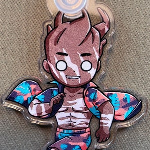 以下が含まれることがあります： トロピカル柄のシャツとショートパンツを着た茶色と白の漫画のキャラクター。キャラクターはサーフボードを持っており、幸せな表情をしています。キャラクターは透明なキーホルダーに取り付けられています。