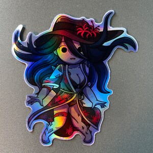 May include: A holographic sticker featuring a cartoon woman with long blue hair wearing a red and black kimono with a flower in her hair. The sticker has a shiny, iridescent finish.