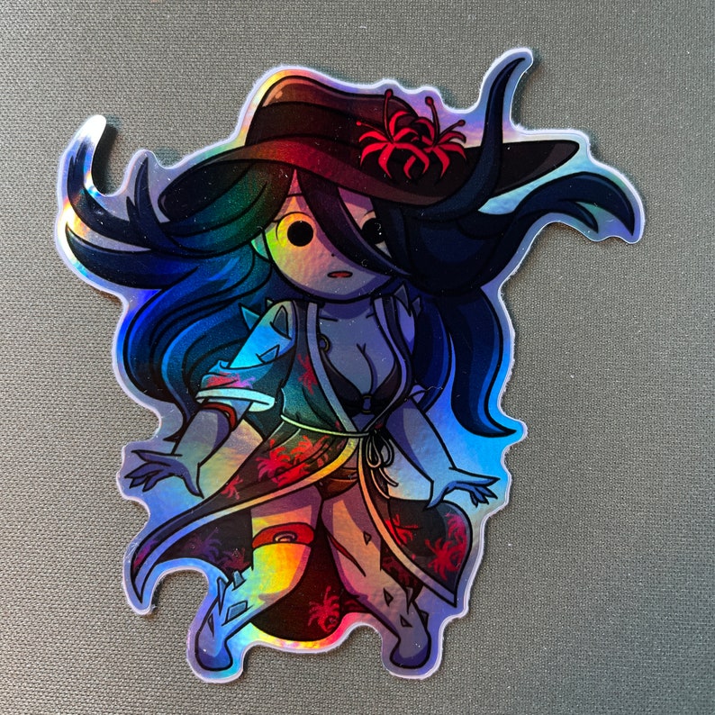 May include: A holographic sticker featuring a cartoon woman with long blue hair wearing a red and black kimono with a flower in her hair. The sticker has a shiny, iridescent finish.