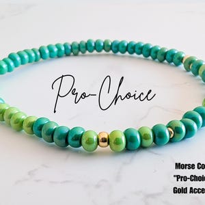 May include: Green and gold beaded bracelet with the Morse code for "Pro-Choice" spelled out in gold beads.