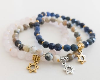May include: Three beaded bracelets with gold accents and star of David charms. The bracelets are made with pink, blue, and brown beads.
