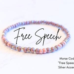 May include: A beaded bracelet in shades of purple and pink, with silver accents. The bracelet spells out "Free Speech" in Morse code. The image also includes the text "Morse Code 'Free Speech' Silver Accents."