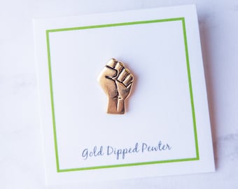 May include: Gold-dipped pewter raised fist pin. The pin is on a white card with a green border and the text "Gold Dipped Pewter".