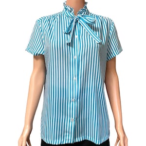 May include: A short-sleeved blouse with vertical stripes in teal and white. The blouse features a ruffled collar and a matching teal bow. It has a button-down front and is made of a lightweight fabric.