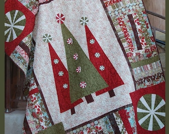 May include: A Christmas-themed quilt featuring a central design of three Christmas trees in red and green, adorned with snowflakes. The quilt has a cream background with red speckles and is bordered by patterned fabric. The text "Step Into Christmas" is visible.