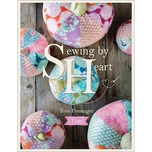 May include: A book cover with the title "Sewing by Heart" and the author's name, Tone Finnanger. The cover features several colorful, patchwork fabric pincushions in shades of pink, orange, blue, and purple. The Tilda logo is also visible.