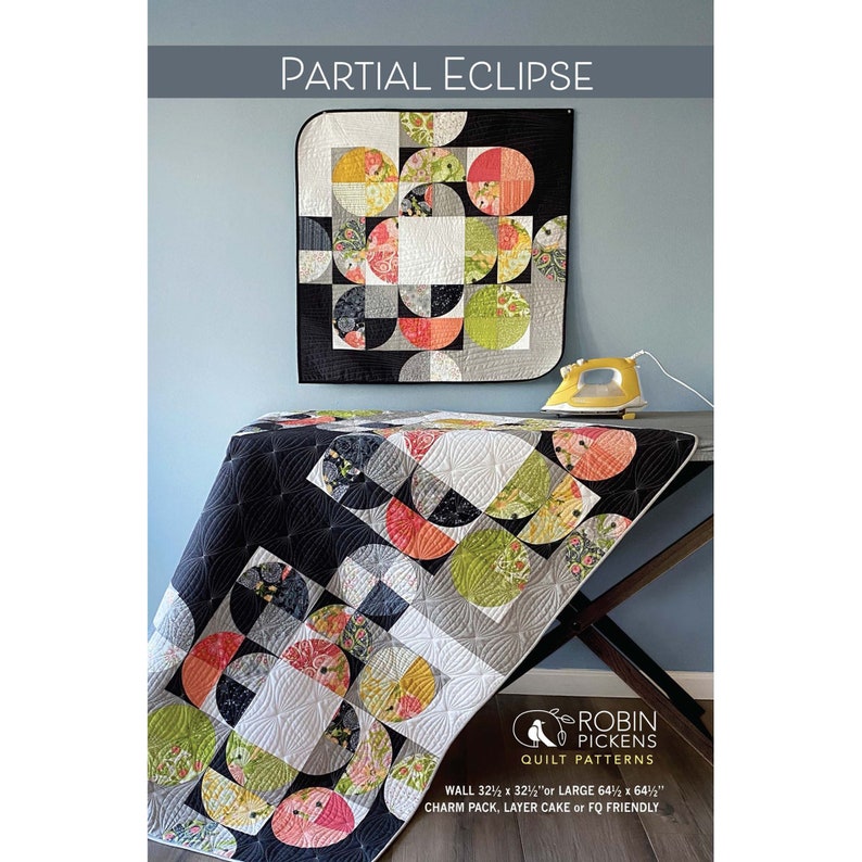 May include: A quilt with a partial eclipse design, featuring semi-circles in various colors and patterns. The quilt is displayed on a table with an iron. The text "PARTIAL ECLIPSE" is at the top. The quilt is 32.5 x 32.5 inches or 64.5 x 64.5 inches.