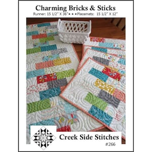 May include: A quilted table runner and placemats with a colorful brick pattern. The runner measures 15 1/2" x 36", and the placemats are 15 1/2" x 12". The design includes a white basket. The text "Charming Bricks & Sticks" is at the top.