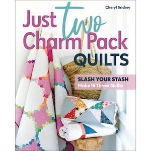 May include: A book cover titled "Just Two Charm Pack Quilts" with a white background. The cover features a pink and white quilt, a woven basket, and a stack of quilts. The text "Slash Your Stash" and "Make 16 Throw Quilts" are also visible.