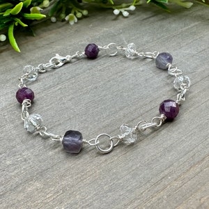 May include: A silver chain bracelet with clear crystal beads and purple amethyst beads.