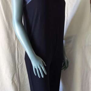 May include: A black jumpsuit with a blue trim around the neckline. The jumpsuit has thin straps and a straight leg.
