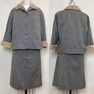 May include: A vintage gray wool skirt suit with a matching jacket. The jacket features a fur collar and cuffs, and decorative buttons. The skirt is knee-length. The suit is displayed on a mannequin.