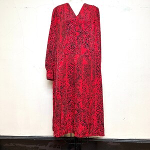 May include: A long-sleeved, knee-length dress with a V-neck. The dress features a bold pattern of black lines against a vibrant red background. The dress is displayed on a mannequin, showcasing its shape and design.