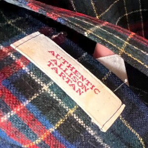 May include: A close-up of a tartan fabric with a label reading "AUTHENTIC ALLISON TARTAN" in red. The plaid design incorporates blue, green, red, and white lines. The label is white with a stitched edge.