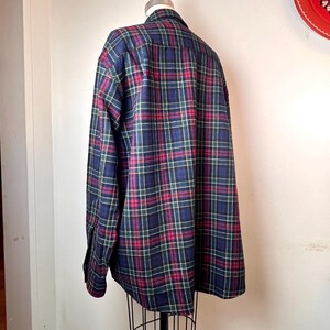 May include: A long-sleeved plaid shirt in a classic pattern. The shirt features a navy blue base with red, green, and white intersecting lines. The shirt is displayed on a mannequin, showcasing the back view of the garment.