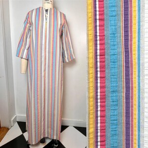 May include: A vintage, floor-length dress with vertical stripes in various colors, including blue, pink, yellow, and purple. The dress has a zipper closure and three-quarter sleeves. The fabric appears to be a lightweight woven material.