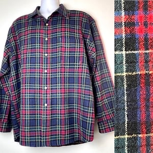 May include: A long-sleeved plaid shirt with a traditional design. The shirt has a button-down front, a collar, and a chest pocket. The plaid pattern includes navy blue, red, green, and white lines. The shirt is displayed on a mannequin.
