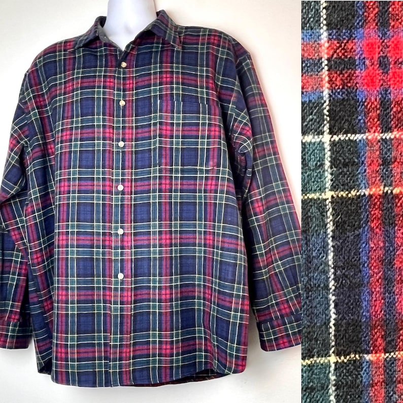 May include: A long-sleeved plaid shirt with a traditional design. The shirt has a button-down front, a collar, and a chest pocket. The plaid pattern includes navy blue, red, green, and white lines. The shirt is displayed on a mannequin.