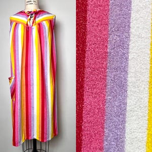May include: A sleeveless, knee-length dress with vertical stripes in red, pink, yellow, and lavender. The dress has a tie at the neckline and a pocket on the side. The fabric appears to be soft and lightweight, perfect for warm weather.