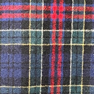 May include: A close-up shot of a tartan fabric. The pattern is a grid of intersecting lines in dark blue, red, green, and yellow. The fabric has a textured surface, possibly wool or a similar woven material.