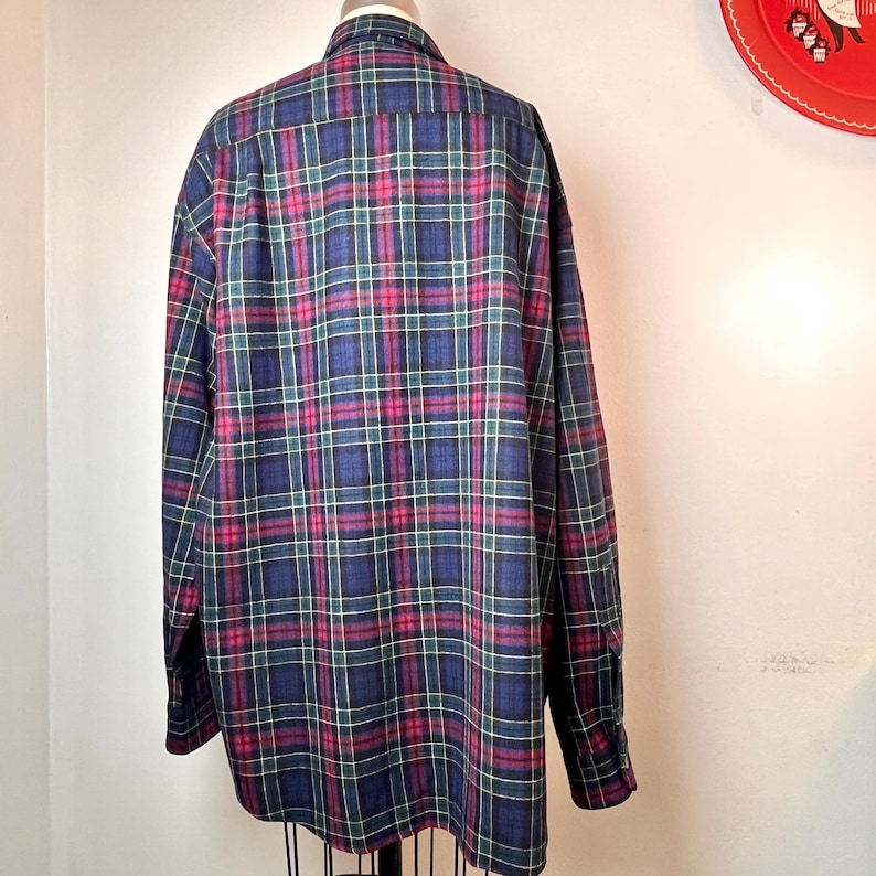 May include: A long-sleeved plaid shirt in a classic pattern. The shirt features a navy blue base with red, green, and yellow intersecting lines. The shirt is displayed on a mannequin, showcasing its full shape and design.