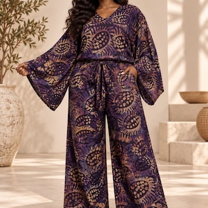 May include: A two-piece set consisting of a V-neck top with wide, flared sleeves and matching wide-leg trousers. The garment features a dark purple and black batik-style print with golden-brown circular patterns and a tie-waist belt.