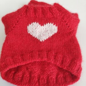 May include: Red knitted sweater with a white heart design. The sweater is made of a soft, fuzzy yarn.