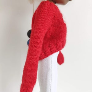 May include: Red knitted sweater with long sleeves. The sweater is a cropped style and has a ribbed texture.