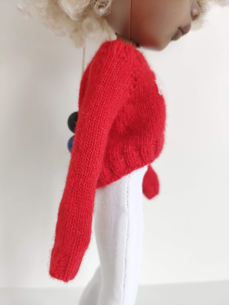 May include: Red knitted sweater with long sleeves. The sweater is a cropped style and has a ribbed texture.
