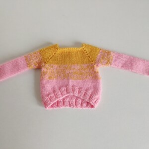 May include: A pink and yellow knitted sweater with a round neckline and long sleeves.