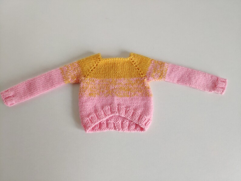 May include: A pink and yellow knitted sweater with a round neckline and long sleeves.