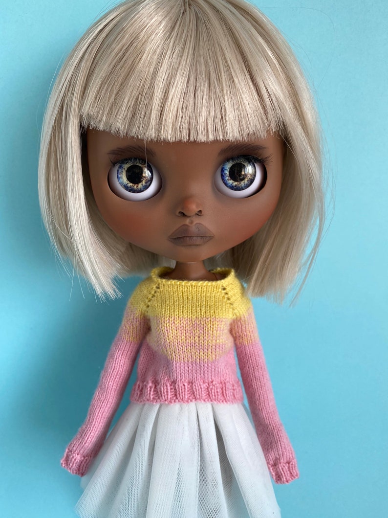 May include: A doll with blonde hair and brown skin wearing a pink and yellow striped sweater and a white tulle skirt.