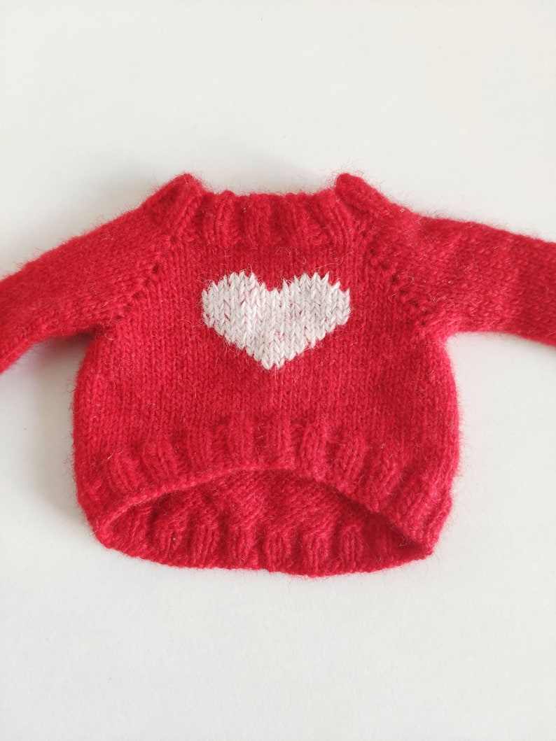 May include: Red knitted sweater with a white heart design.