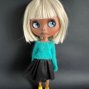 May include: A doll with white hair, blue eyes, and brown skin wearing a teal sweater, a black tulle skirt, and yellow sneakers.