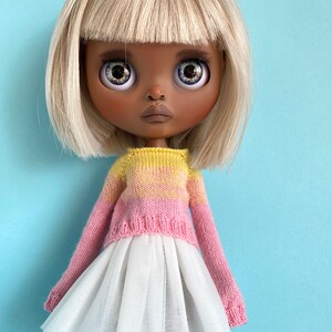 May include: A doll with blonde hair and a pink and yellow knitted sweater, wearing a white tulle skirt.